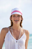 A young brunette woman on a beach wearing a white top and a white hat