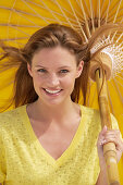 A young brunette woman wearing a yellow shirt holding a parasol