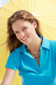 A young brunette woman wearing a blue shirt in front of a yellow parasol