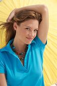 A young brunette woman wearing a blue shirt in front of a yellow parasol