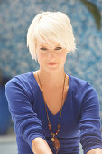 A mature blonde woman with short hair wearing a blue top against a blue background