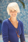 A mature blonde woman with short hair wearing a blue top against a blue background