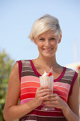 A mature blonde woman with short hair outside wearing a striped top holding a cold drink