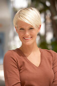 A mature blonde woman with short hair outside wearing a brown top with sunglasses on her head