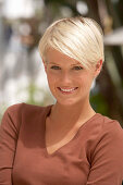 A mature blonde woman with short hair outside wearing a brown top