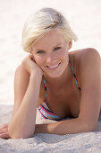 A mature blonde woman with short hair on a beach wearing a striped bikini