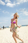 A young blonde woman on a beach wearing a purple bikini with a towel around her hips