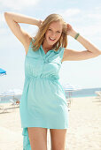 A young blonde woman on a beach wearing a light-blue summer dress