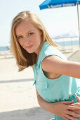 A young blonde woman on a beach wearing a light-blue summer dress