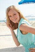 A young blonde woman on a beach wearing a light-blue summer dress