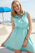 Junge blonde Frau im hellblauen Sommerkleid am Strand