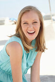 A young blonde woman on a beach wearing a light-blue summer dress