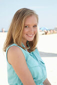 Junge blonde Frau im hellblauen Sommerkleid am Strand
