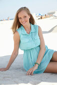 A young blonde woman on a beach wearing a light-blue summer dress