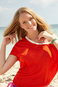 A young blonde woman on a beach wearing a purple bikini and an orange top