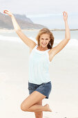 A young blonde woman on a beach wearing a light-blue top and a denim skirt