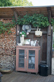Crockery in antique cabinet with vase of geraniums on top