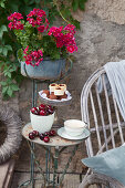 Bowl of cherries, coffee cup and pastries on cake stand on small vintage table on terrace