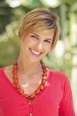 A mature woman with short blonde hair outside wearing a red shirt