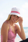 Junge blonde frau im rot-weiß gestreiften Shirt und mit weißem Hut am Strand