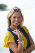 A young blonde woman on a beach wearing a yellow top and a denim waistcoat