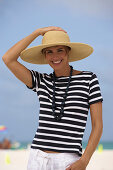 A young blonde woman with short hair on a beach wearing a black-and-white striped top and a beige hat
