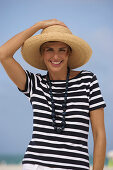 A young blonde woman with short hair on a beach wearing a black-and-white striped top and a beige hat