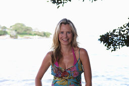 A young blonde woman on a beach wearing a purple bikini top and a summer dress