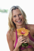 A young blonde woman wearing a purple bikini top holding a flower