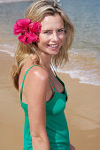 A young blonde woman with flower in hair wearing a green top on a beach