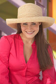 A young brunette woman wearing a dark pink blouse and a summer hat