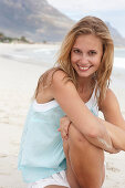 A young blonde woman on a beach wearing a light-blue top