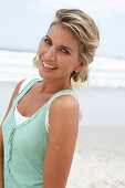 Reife blonde Frau im weißen Top und türkisfarbener Weste am Strand