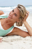 A mature blonde woman on a beach wearing a white top and a turquoise vest