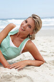 A mature blonde woman on a beach wearing a white top and a turquoise vest