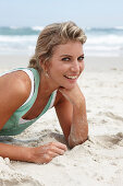 A mature blonde woman on a beach wearing a white top and a turquoise vest