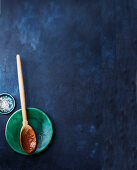 A used wooden spoon in a bowl on a blue surface