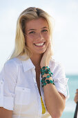 A young blonde woman on a beach wearing a white blouse