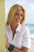 A young blonde woman on a beach wearing a white blouse