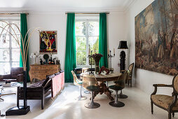 Runder Holztisch mit Klassikerstühlen vor großformatigem Gemälde, Ledergarnitur und Holzkommode im Wohnzimmer