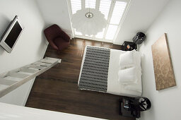 Blick von der Galerie auf Doppelbett und Sessel in weißem Schlafzimmer