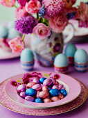 Schokoladen-Ostereier auf rosa Teller, Frühstückseier in Eierbechern und Blumenstrauß