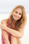 A young blonde woman on a beach wearing a pink top and a bikini