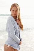 A blonde woman on a beach wearing a white bikini and a light cardigan