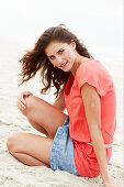 A brunette woman on a beach wearing a salmon-coloured top and a denim skirt