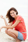 A brunette woman on a beach wearing a salmon-coloured top and a denim skirt