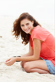 A brunette woman on a beach wearing a salmon-coloured top and a denim skirt