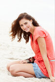 A brunette woman on a beach wearing a salmon-coloured top and a denim skirt