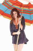 A brunette woman wearing a purple bath robe with a colourful parasol