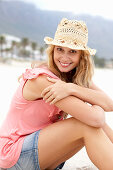 Junge blonde Frau im rosa Top, kurzem Jeansrock und beigem Hut am Strand